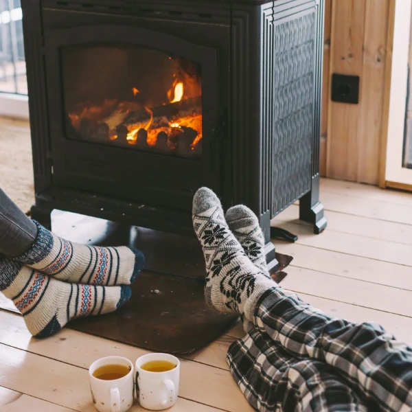 two people with socks on sitting by a fireplace and 2 cups filled with tea